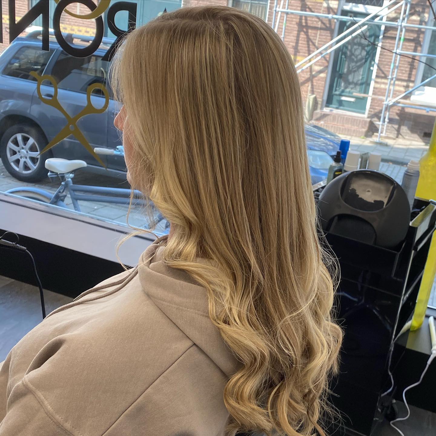 Lang blond golvend haar van opzij, met het gouden Baron-logo op het raam erachter