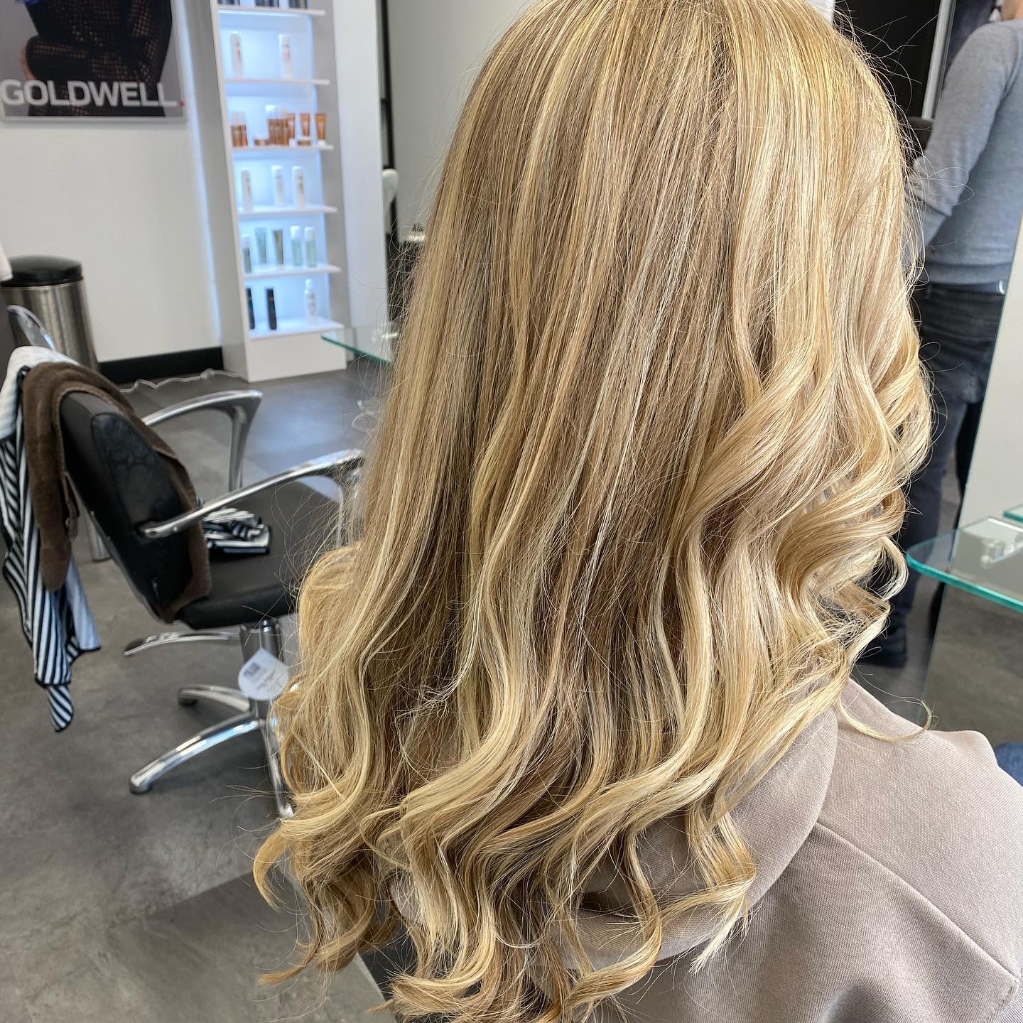 Lang blond golvend haar van achteren gezien, bij een werkplek in de salon
